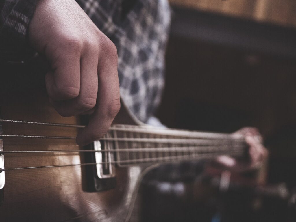 Handen op de snaren van een basgitaar, van dichtbij