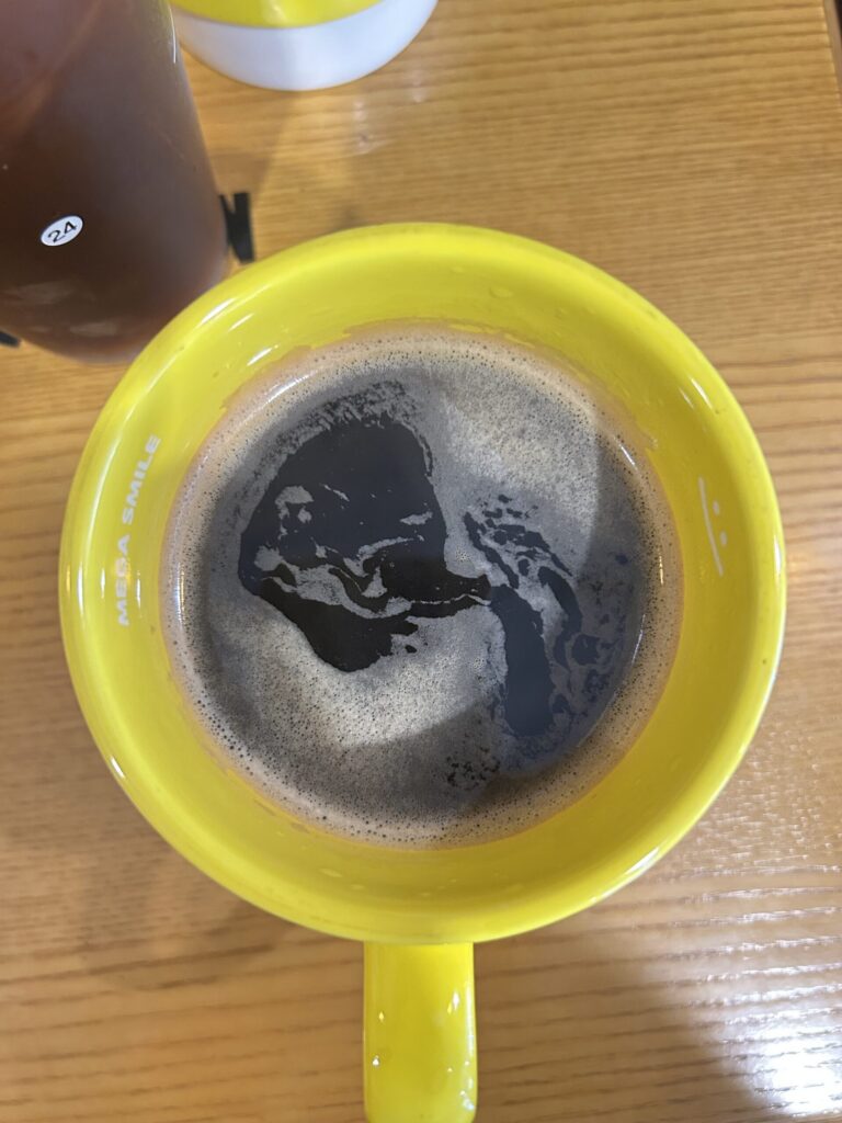 Gele mok met zwarte koffie op een houten tafel, van bovenaf